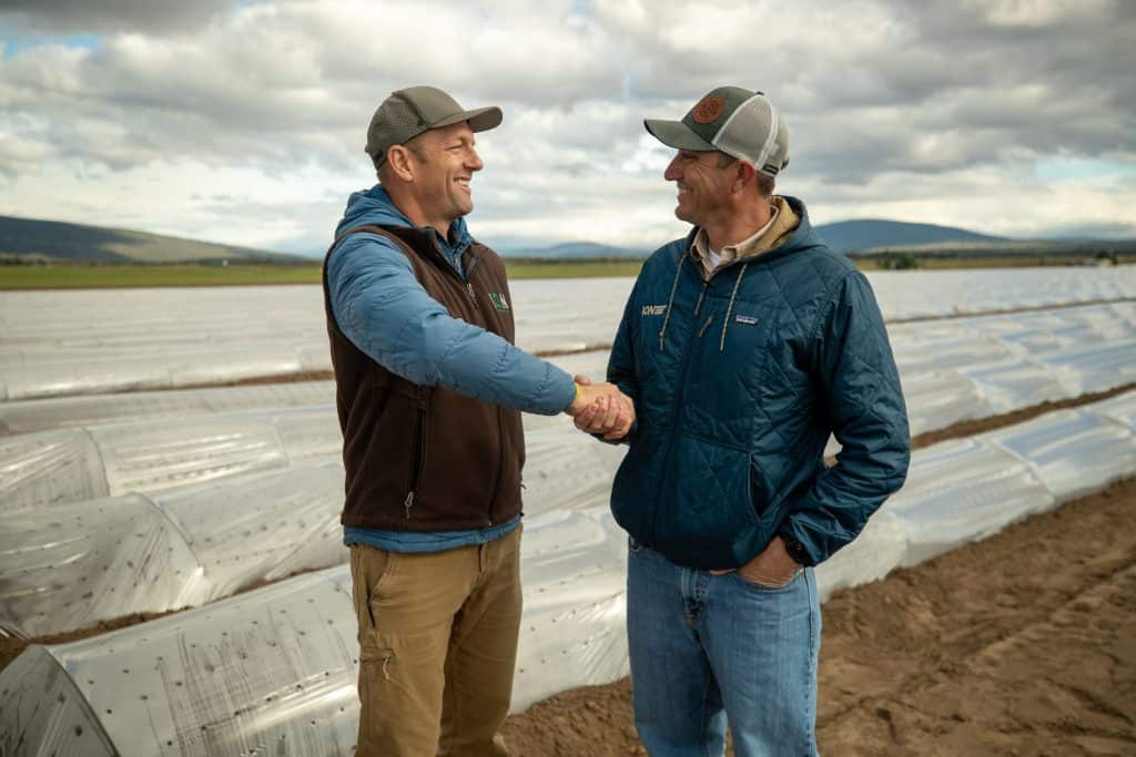 Two farmers shaking hands in an organic nursery with plastic-covered beds.