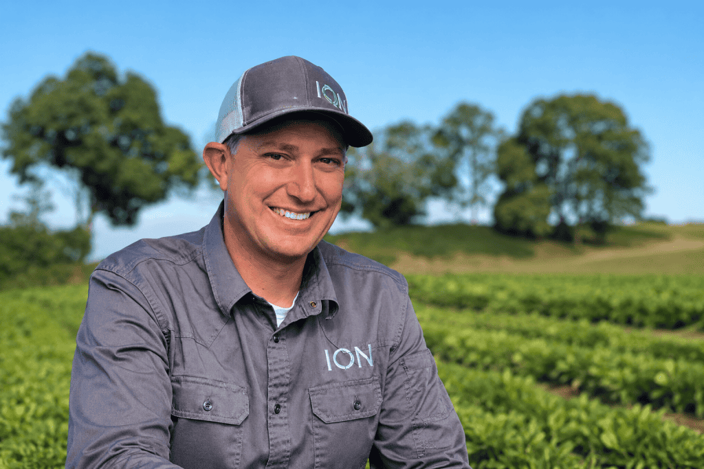 Smiling man in a gray shirt and cap at organic nursery.